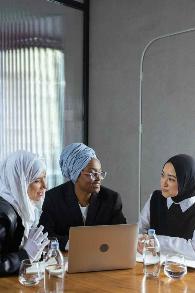 Three businesswomen in hijabs collaborate during a team meeting indoors with a laptop.