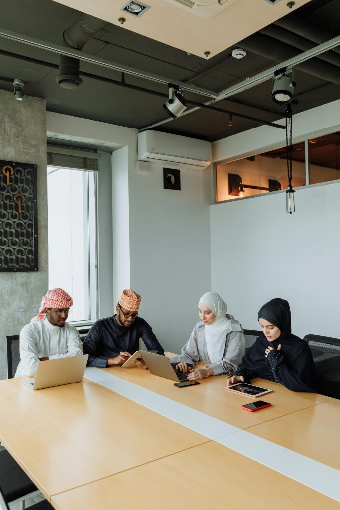 A group of Muslim professionals collaborating in a modern meeting room with laptops and tablets.